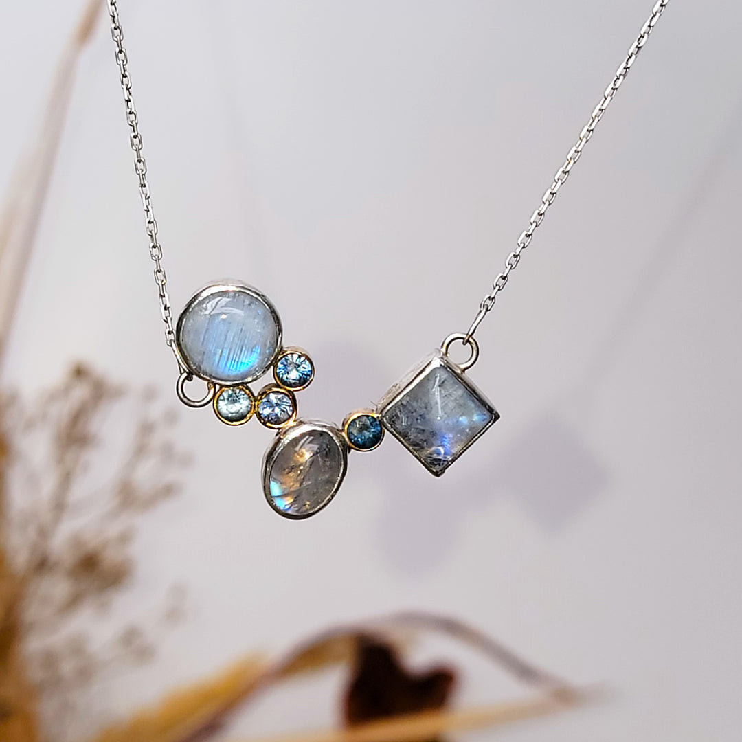moonstone and montana sapphire cluster necklace in front of white background with yellow and red folliage