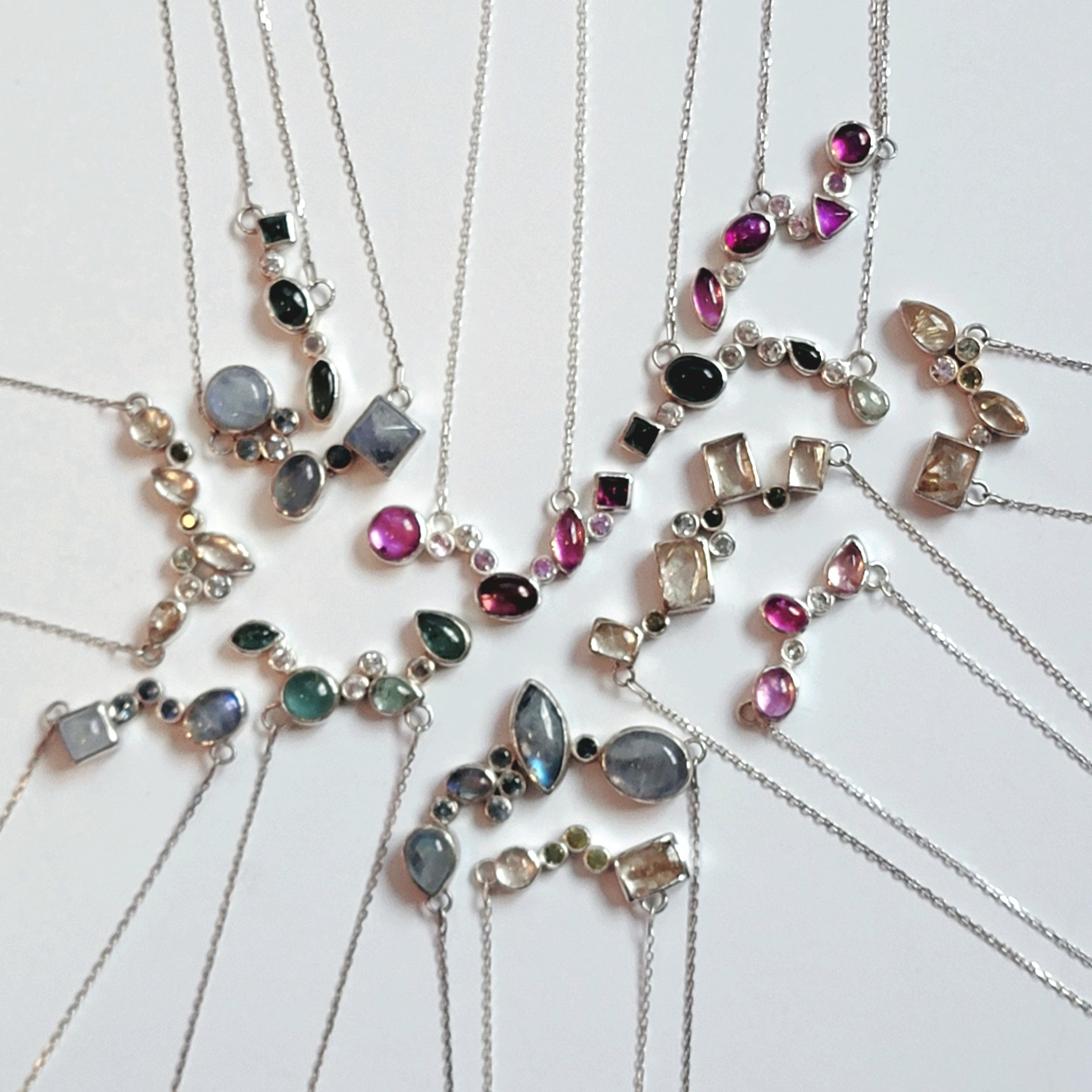 the 13 necklaces that make up the Starry Night Collection laid out on a white background to mimic a night sky