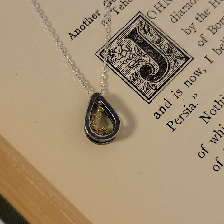 Sterling silver teardrop pendant with 18k yellow gold "lace-like" detail, on cream background.