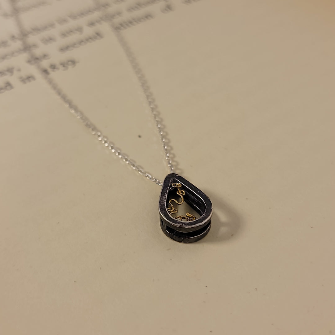 Sterling silver teardrop, with 18k yellow gold "lace-like" detail, on cream background