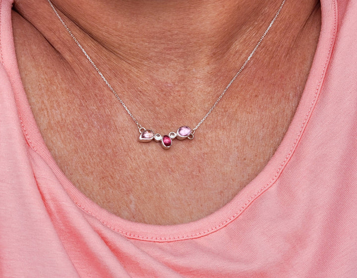 Close up of 5 stone cluster necklace with 2 baby pink tourmalines, 1 magenta pink tourmaline, and 2 white sapphires on model wearing pink shirt.