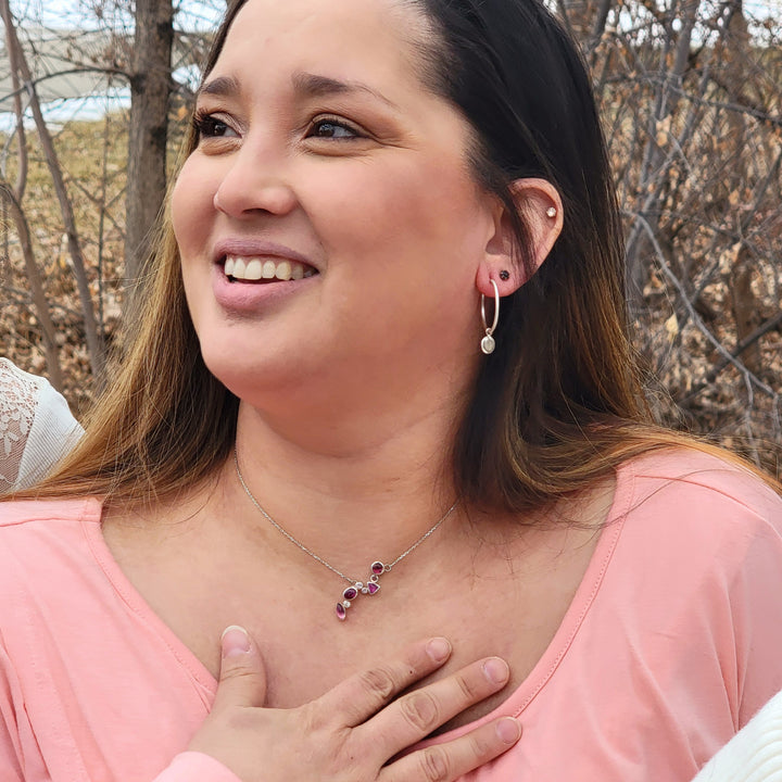one of a kind cluster necklace on model in front of a wooded background. The necklace has 4 magenta pink tourmalines, and 4 white and baby pink sapphires.