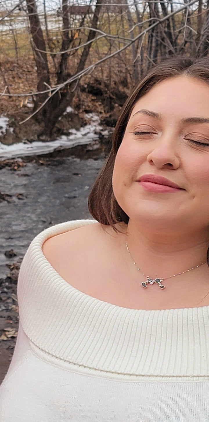 Mint green tourmaline cluster necklace on a model wearing a cream off the shoulder sweater. She is front of a creek and trees.